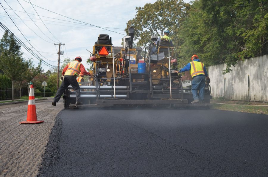 Paving crew laying fresh asphalt on a suburban road with a paving machine and traffic cone